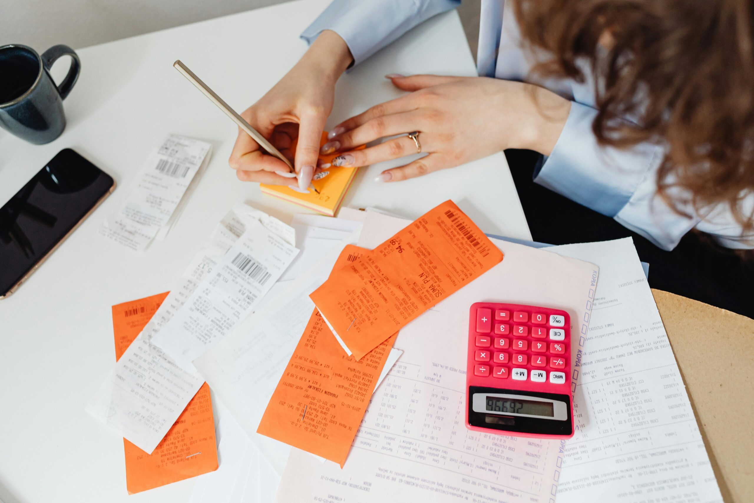 A woman writes down financial details using a calculator, receipts, and documents.